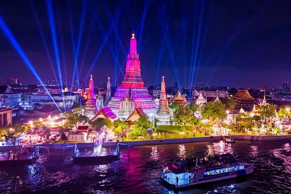 Wat Arun illuminé la nuit par des projecteurs, vu depuis un bateau de croisière sur le Chao Phraya