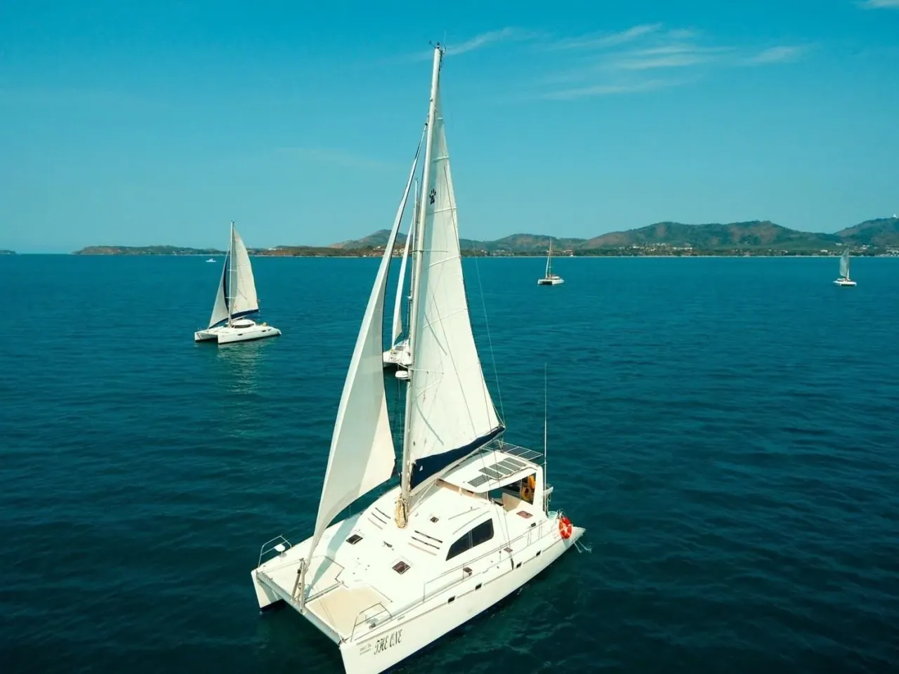 Des catamarans de croisière ancrés dans une eau bleu profond au large d’un promontoire verdoyant de Phuket