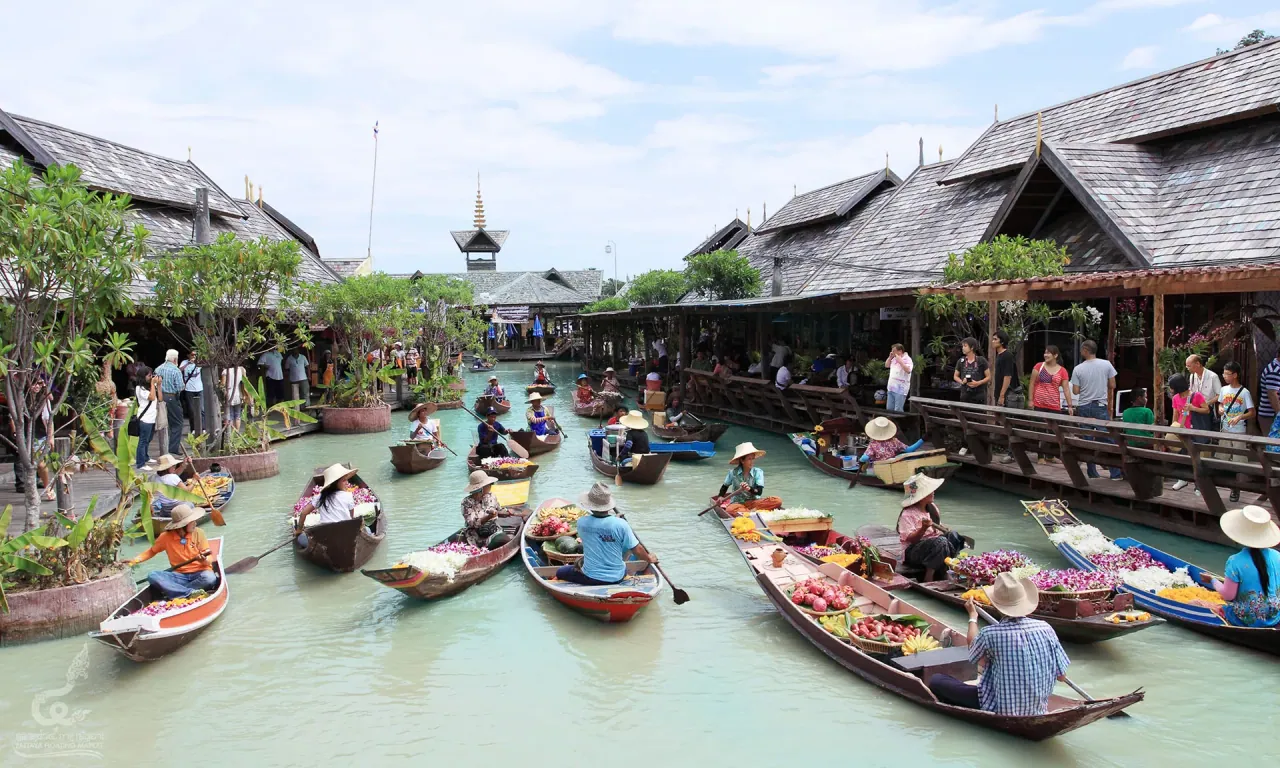 Des vendeurs en chapeaux de paille pagayant sur des barques chargées de fleurs et de fruits le long d’un canal de marché flottant thaïlandais