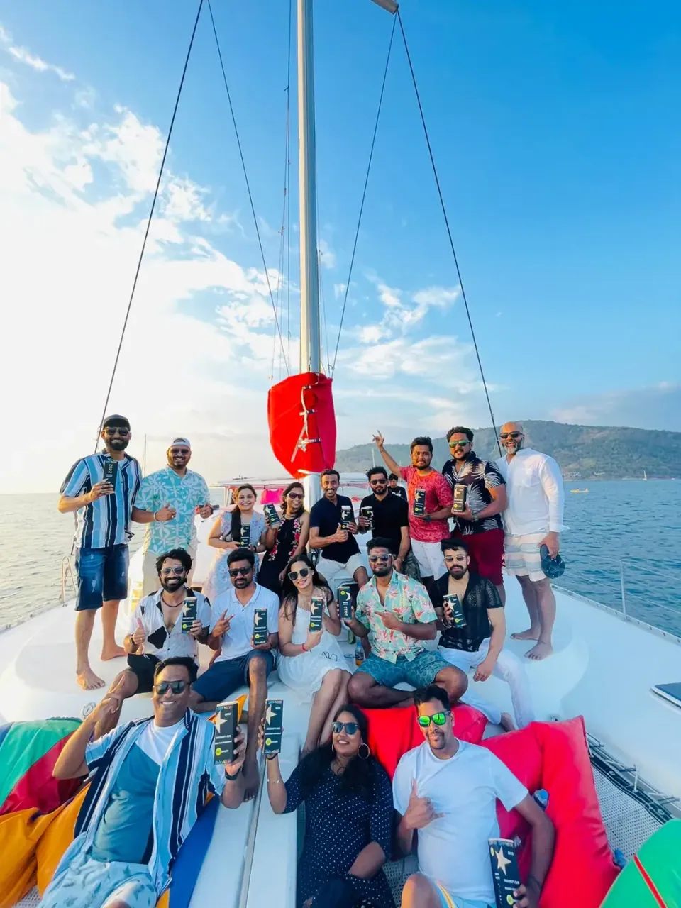 Un grand groupe de participants posant avec leurs trophées à la proue d’un catamaran en mer