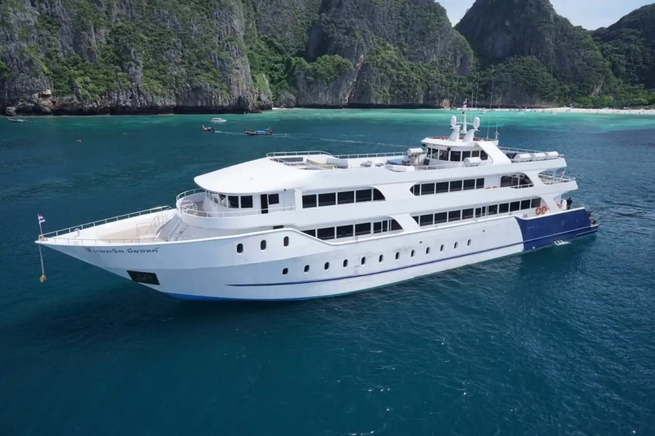 Un bateau de croisière ancré dans une eau turquoise au pied des falaises calcaires couvertes de jungle des îles Phi Phi